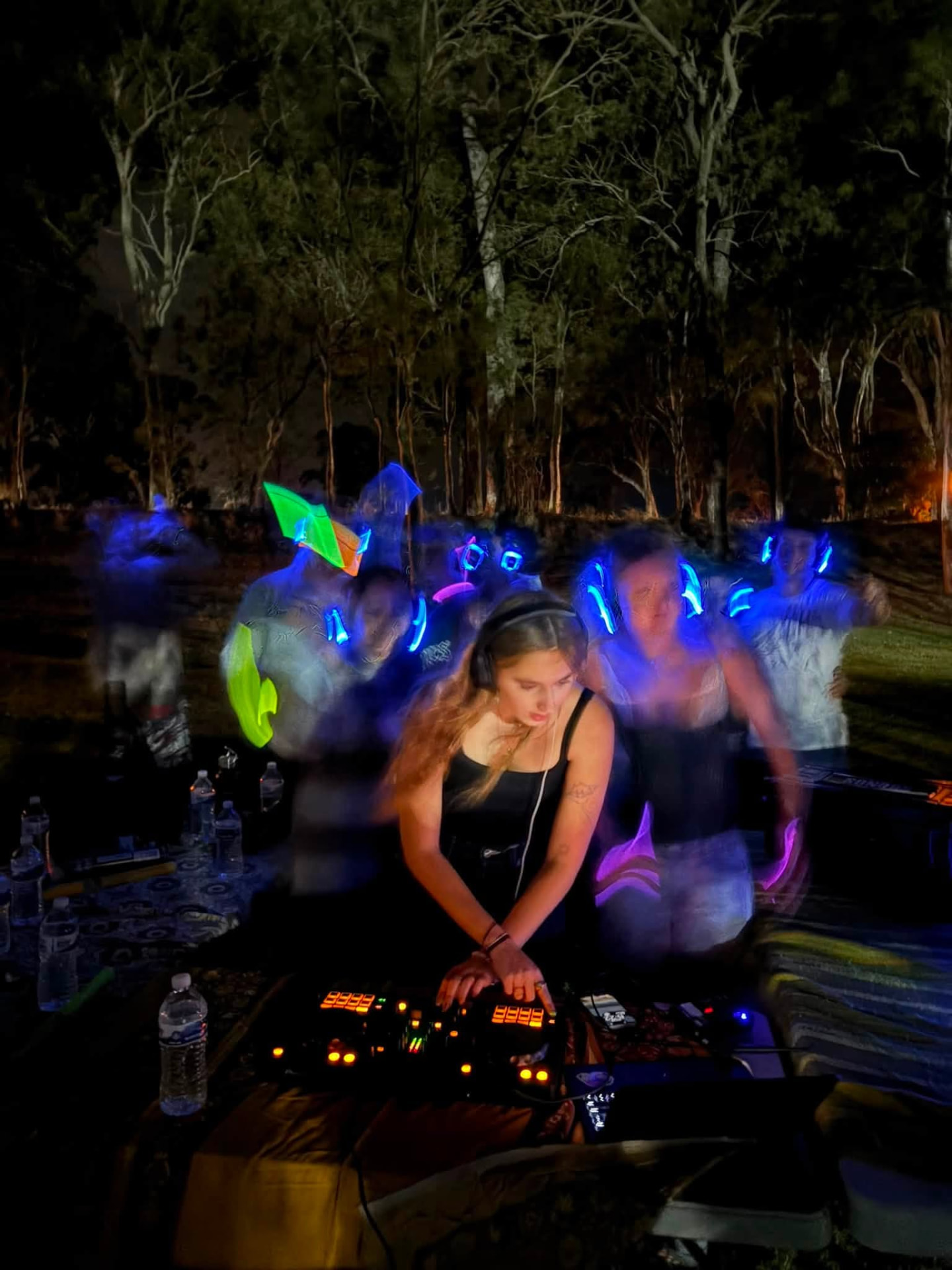 EDN DJ mixing on the decks at night while dancers glow in blue headphones