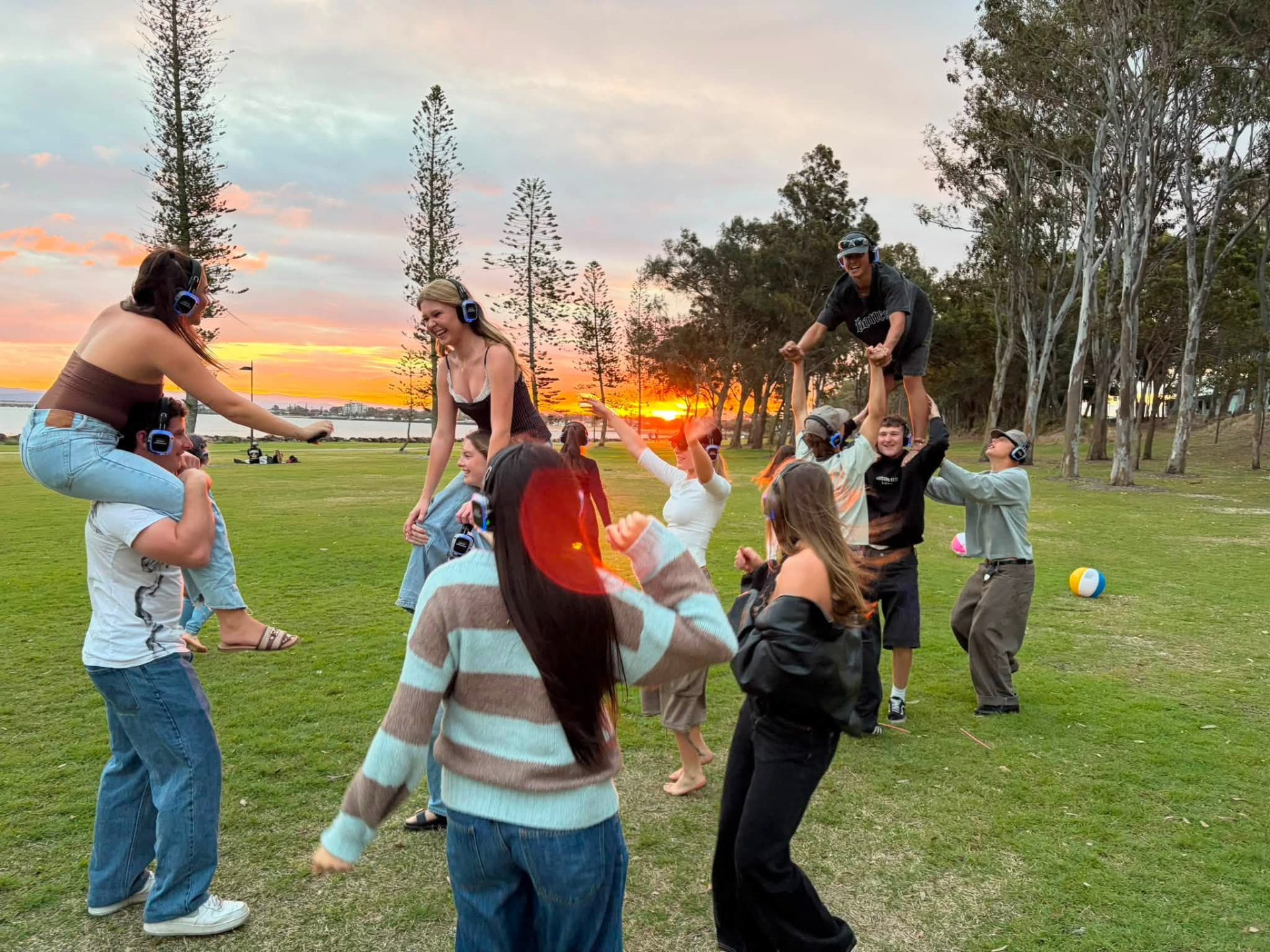 A crowd wearing wireless headphones dancing on the grass as the sun sets over Moreton Bay