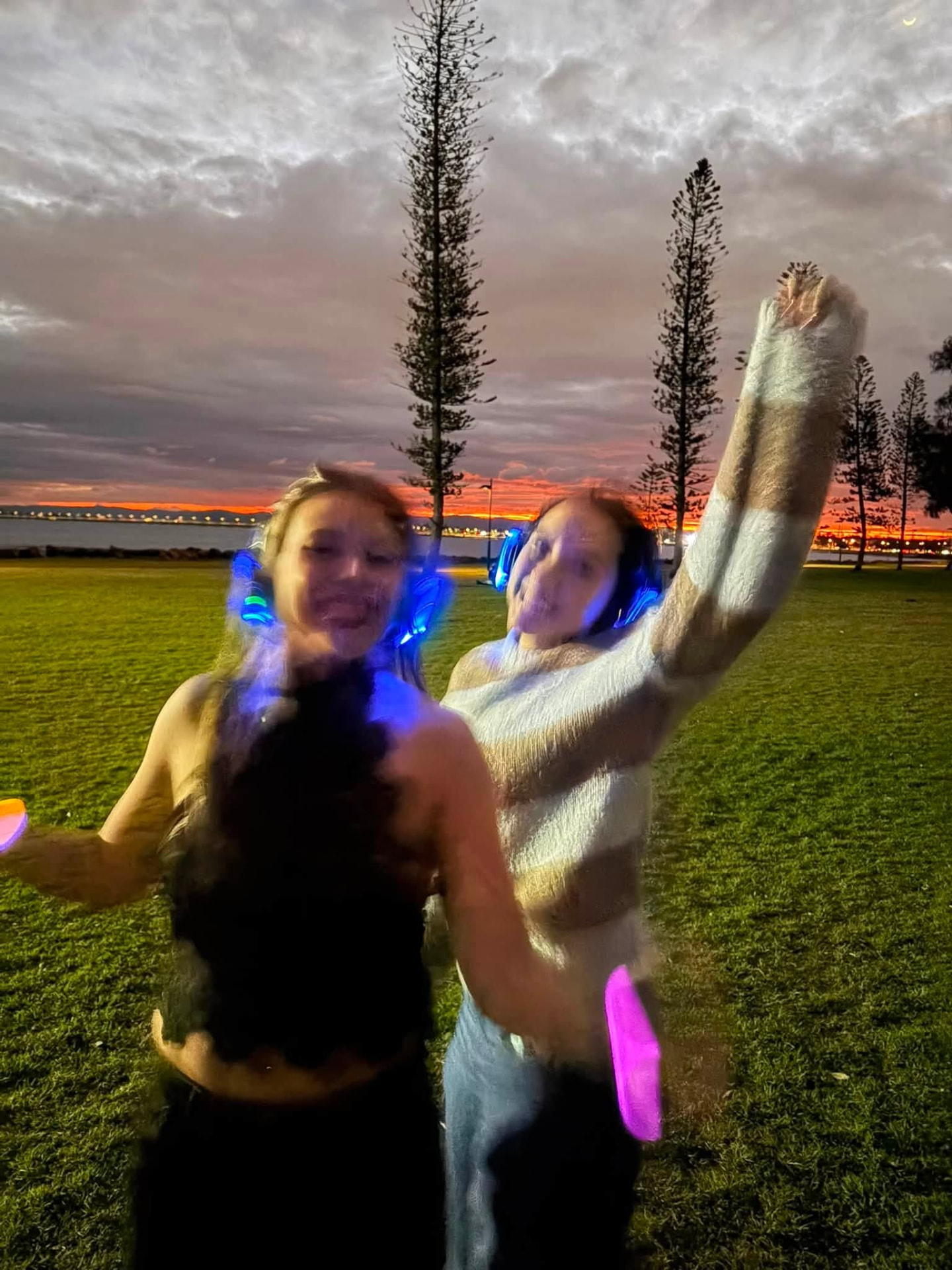 Two friends dancing with headphones as the last light fades over the bay