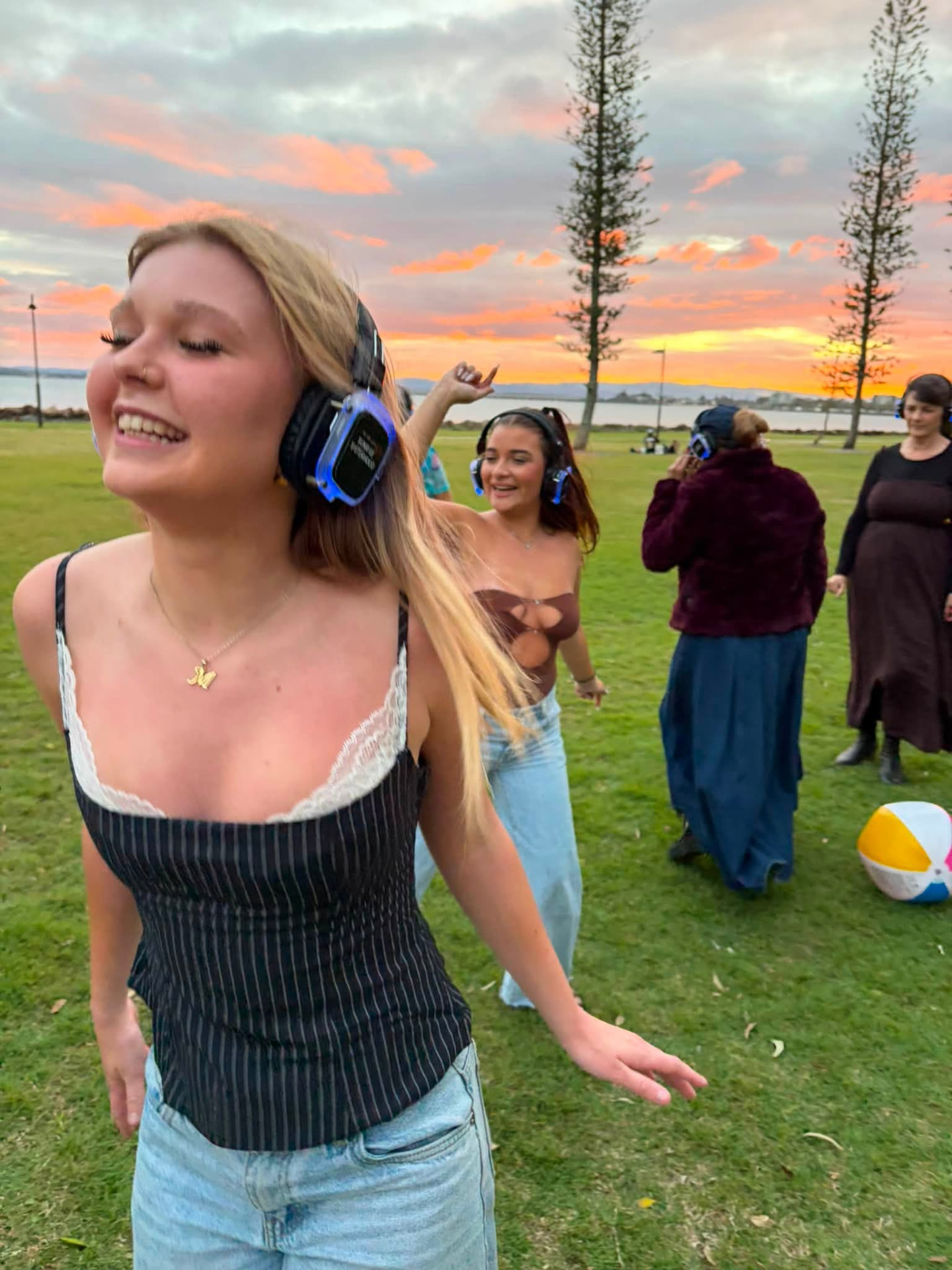 Friends laughing and dancing in glowing headphones under a pink sunset sky